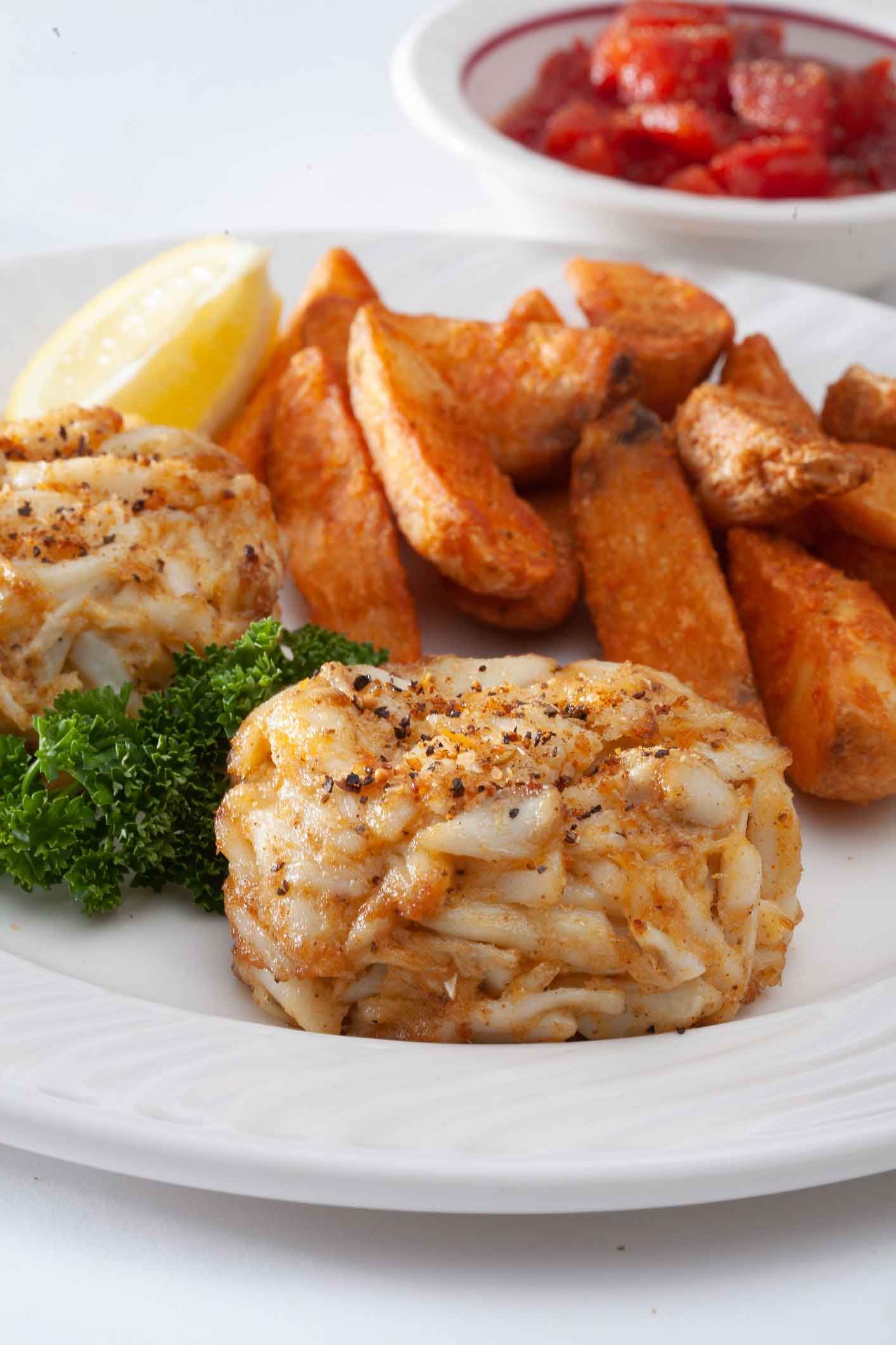 A white plate topped with crab cakes and french fries.