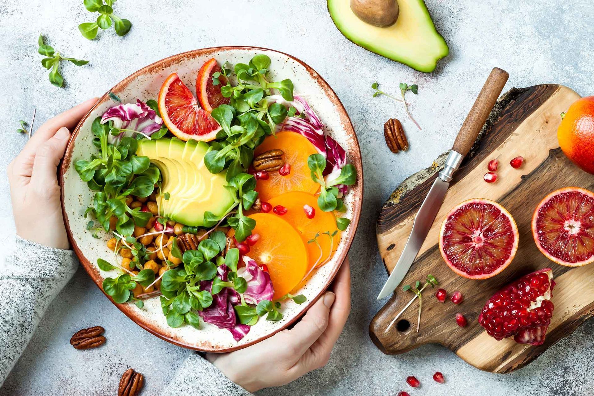 A person is holding a bowl of salad next to a cutting board.