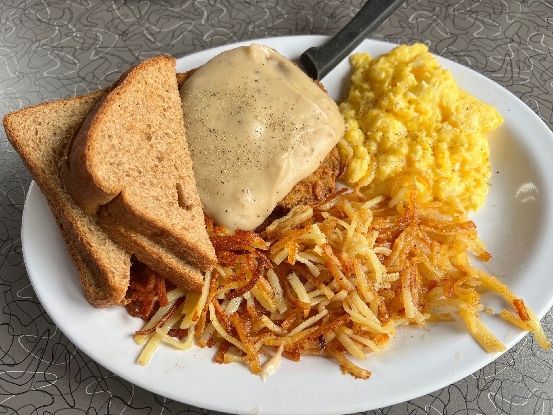 A white plate topped with scrambled eggs , hash browns , toast and gravy.