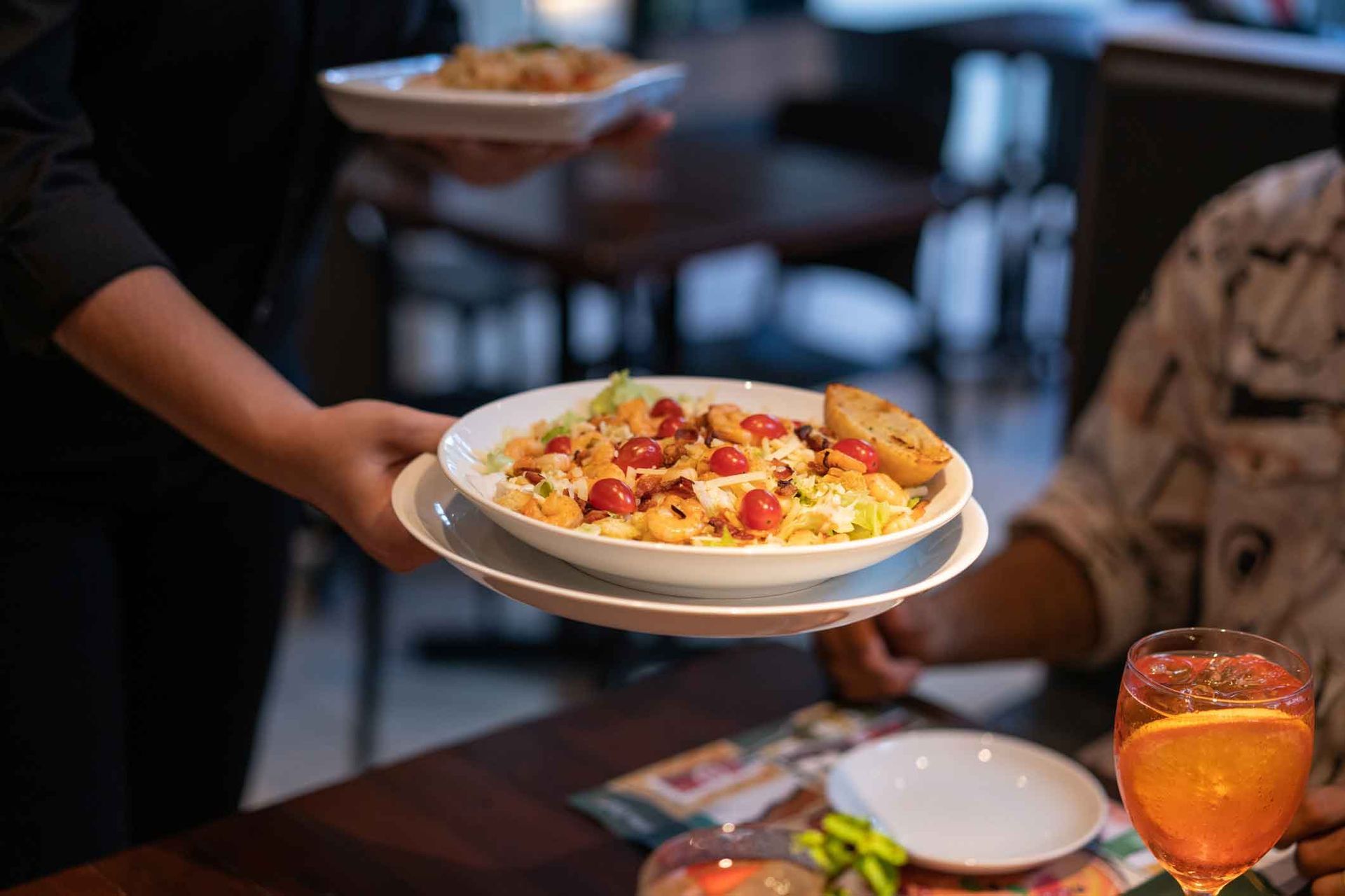 A waitress is carrying a plate of food to a table.