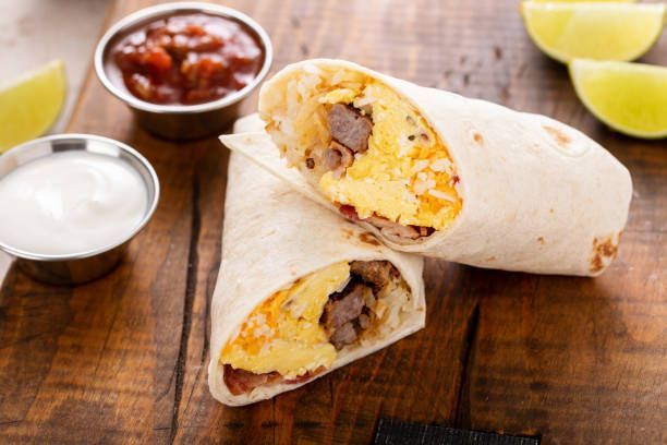 A burrito is cut in half on a wooden table.