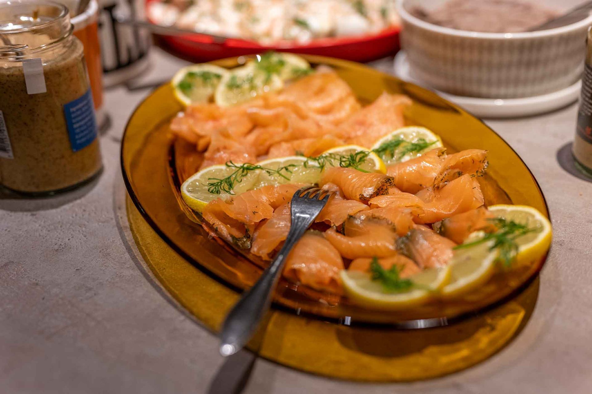 A plate of smoked salmon with lemon slices and a fork on a table.