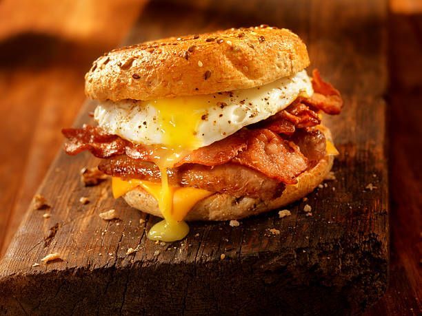 A bacon egg and cheese sandwich on a bagel on a wooden cutting board.
