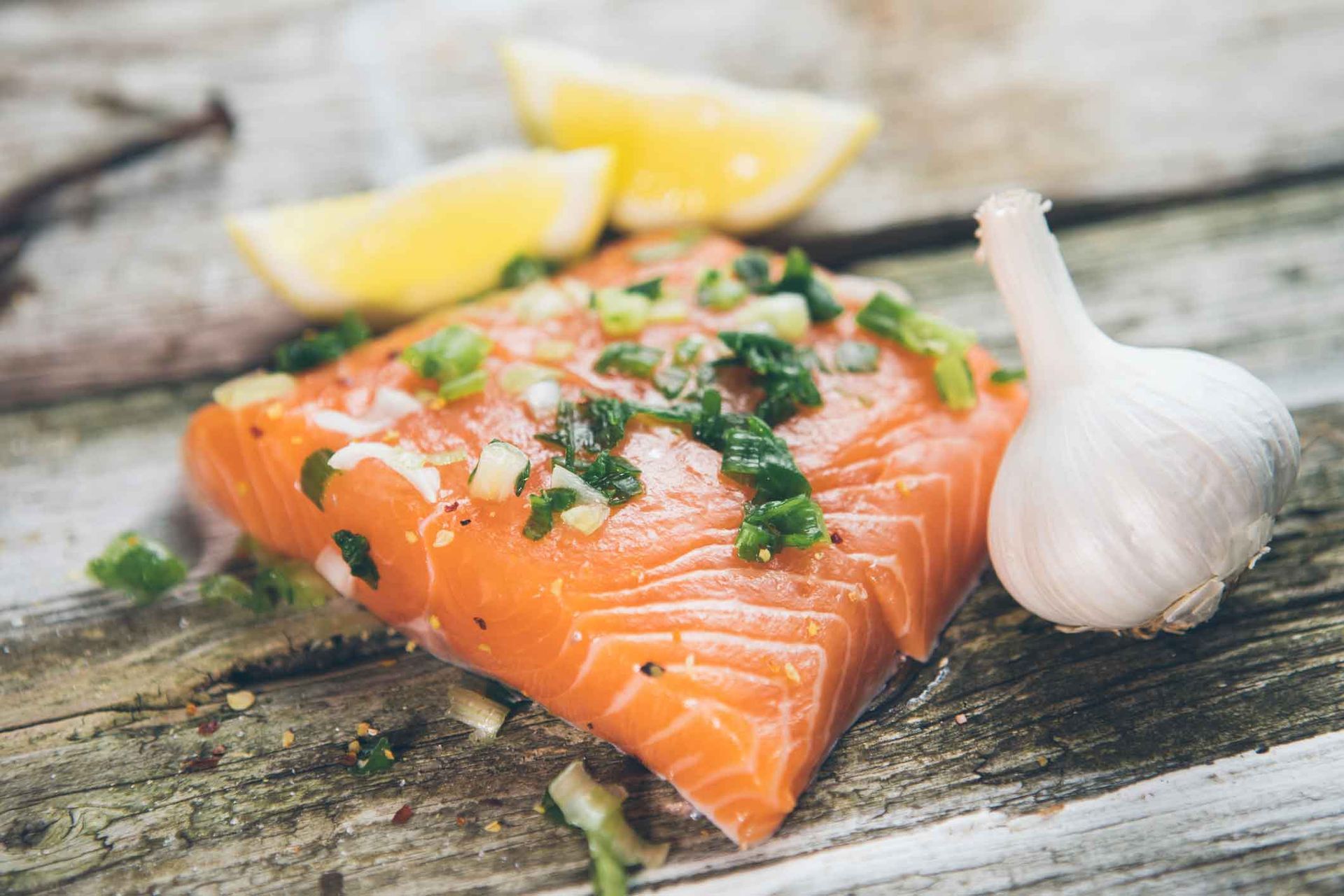 A piece of salmon with garlic and lemon on a wooden table.