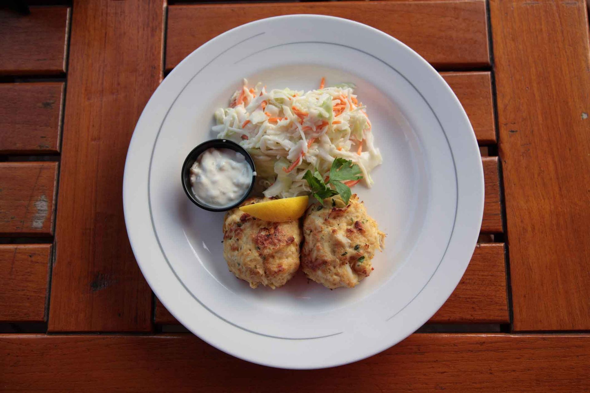 A white plate topped with crab cakes and coleslaw on a wooden table.