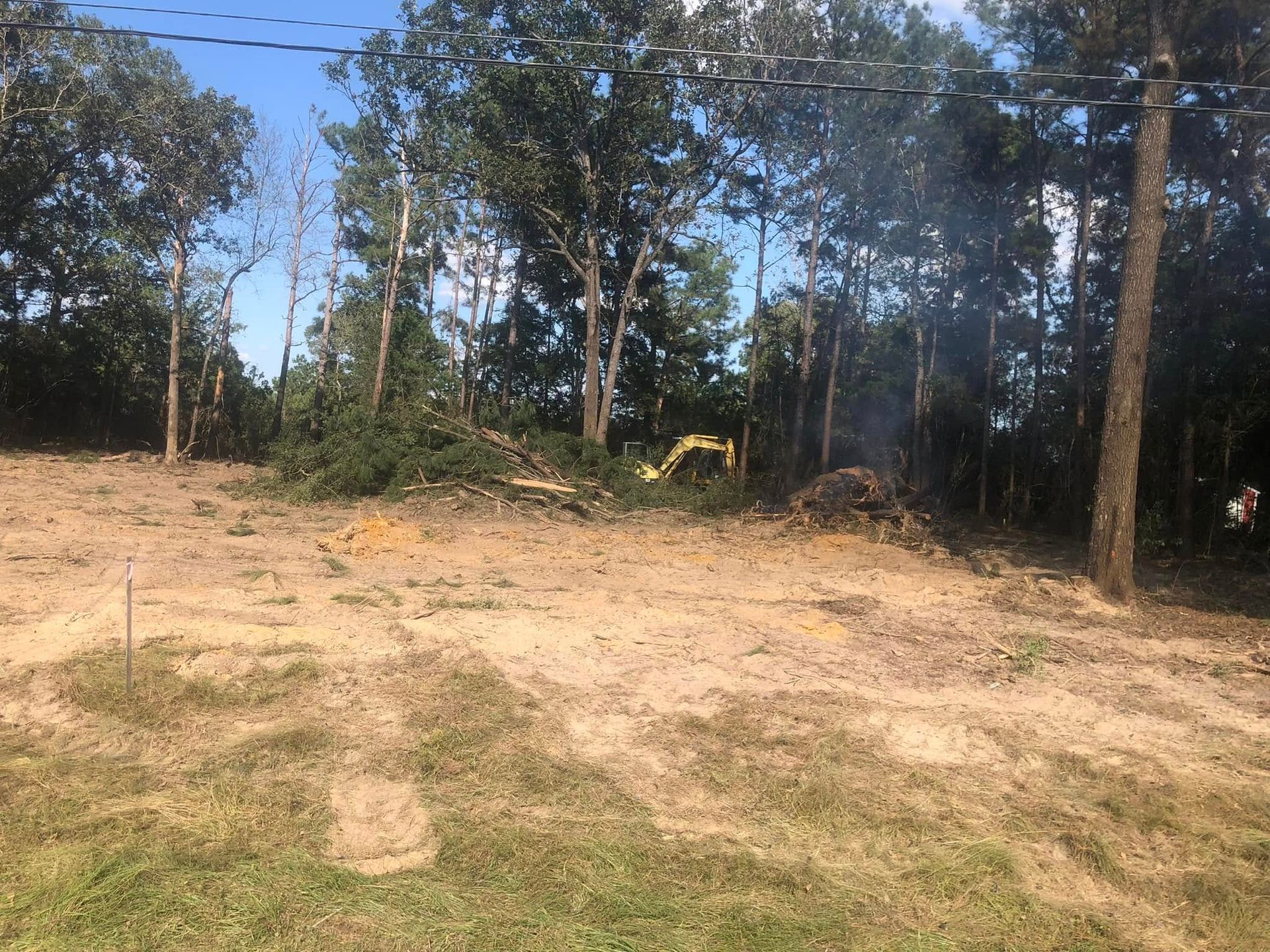 A dirt field with trees in the background and a yellow excavator in the foreground.