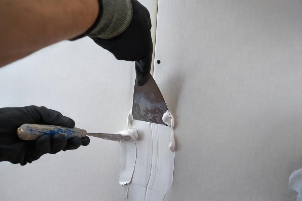 a person is holding a spatula and applying paint to a wall .