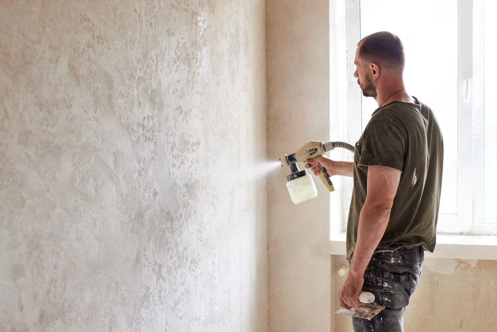 A man is paining wall with white sprayer.