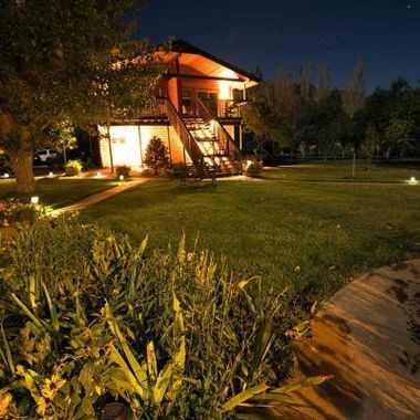 Illuminated house at night with a staircase, lawn, and trees surrounding the yard