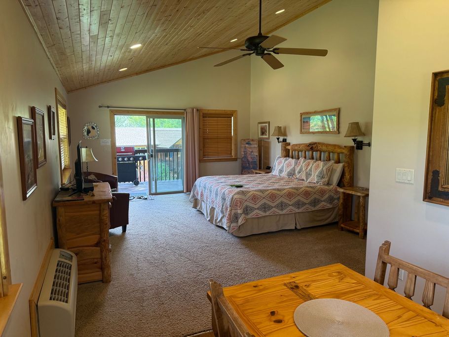 Spacious bedroom with vaulted wood ceiling, king bed, ceiling fan, and sliding doors to a patio.