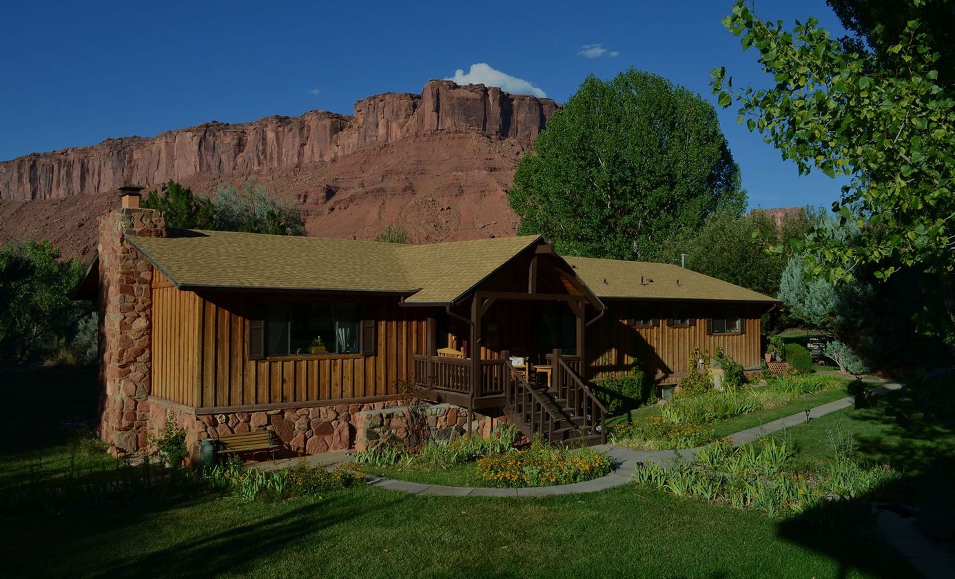 Rustic cabin with green roof and porch in a sunny desert canyon landscape