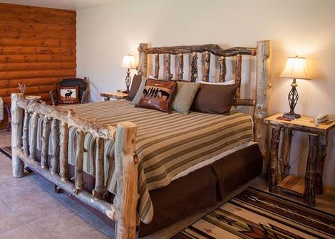 Rustic bedroom with a log bed, striped bedding, and matching wooden nightstands with lamps