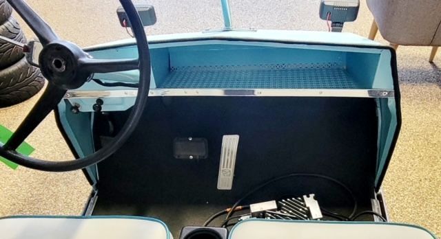 The inside of a golf cart with a steering wheel and seats.