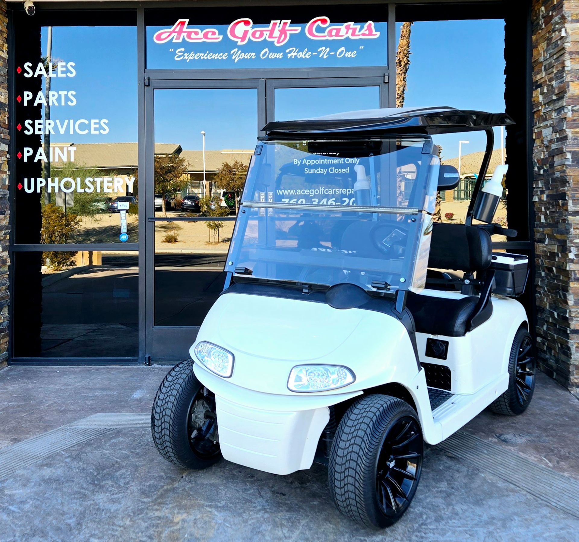 A white golf cart is parked in front of an area golf cars store
