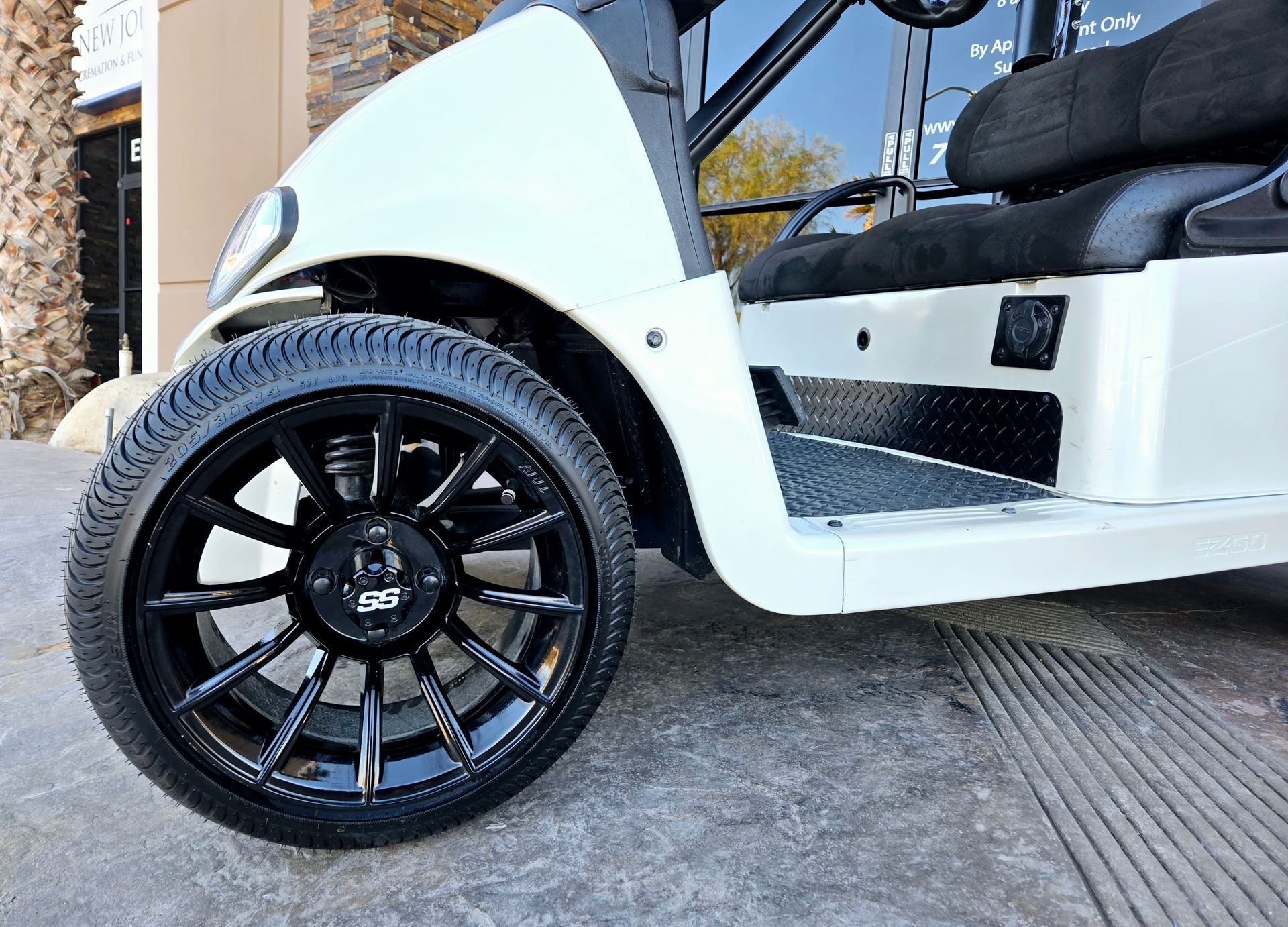 A white golf cart with black wheels and tires is parked on the side of the road.