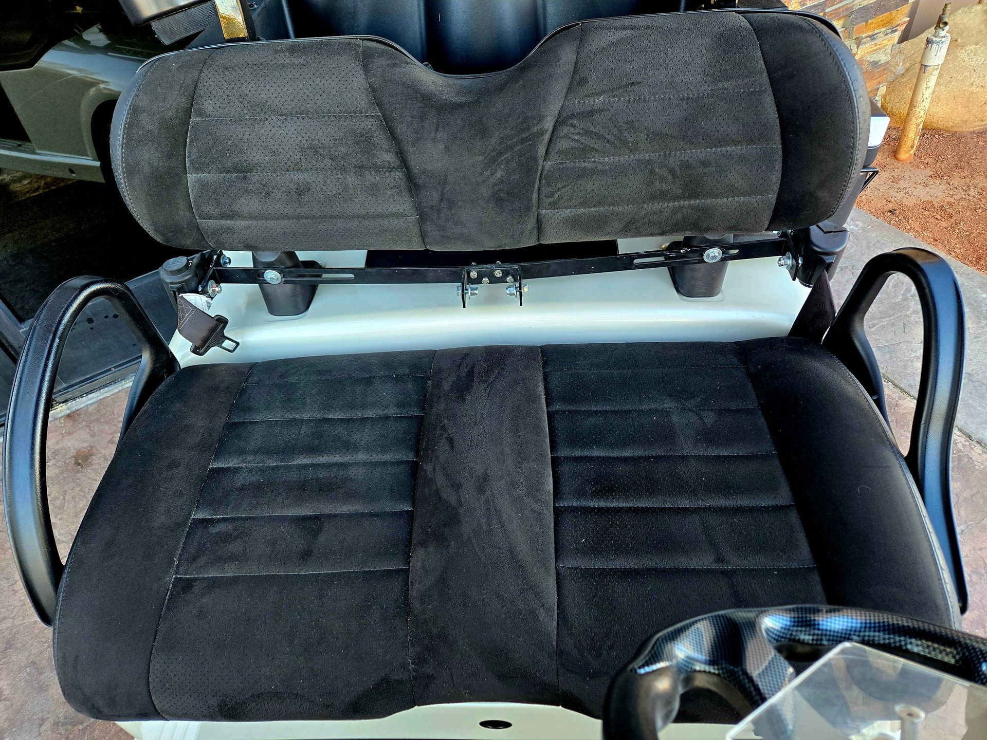 The back seat of a golf cart is black and has a steering wheel.