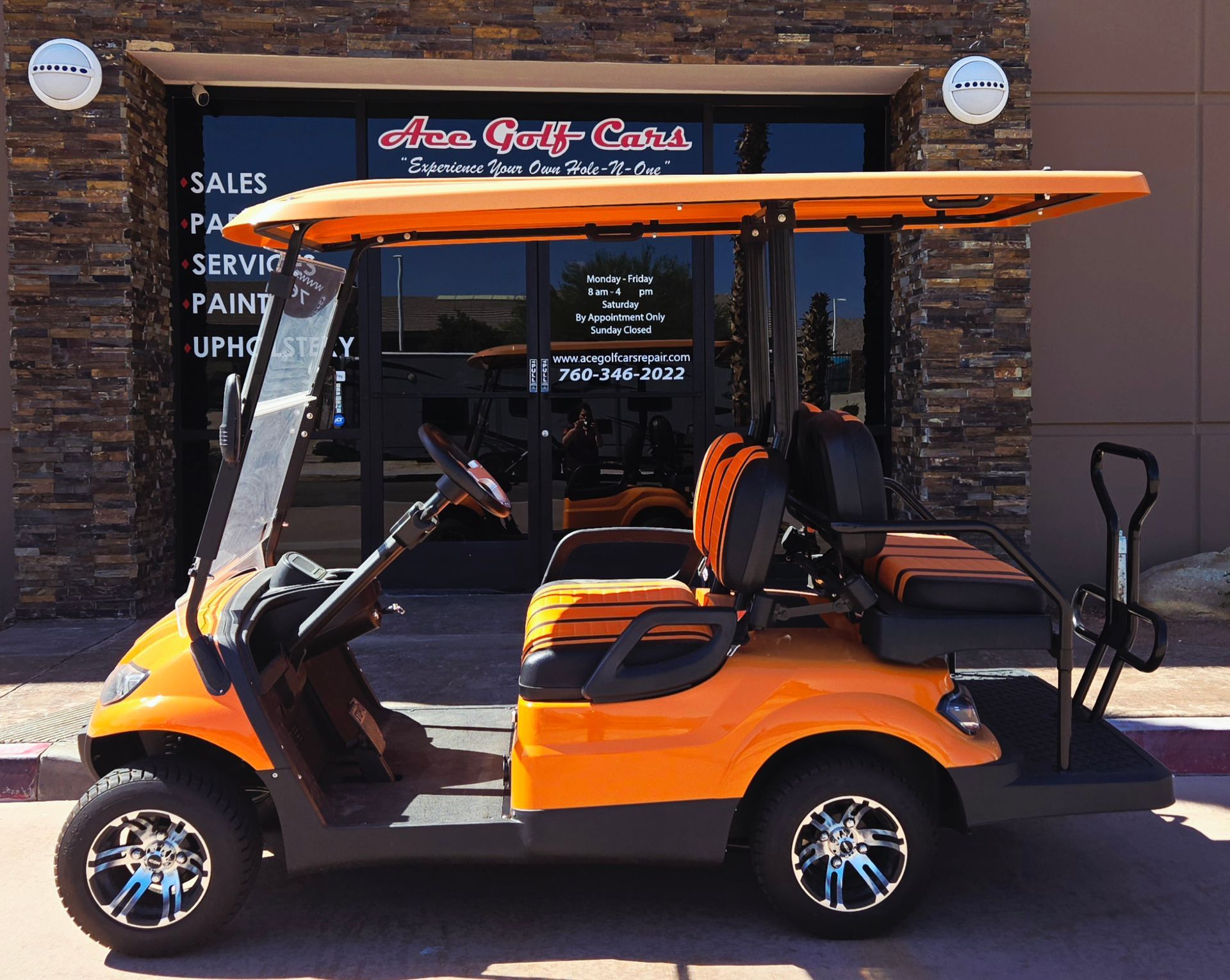 An orange golf cart is parked in front of a store that sells golf carts