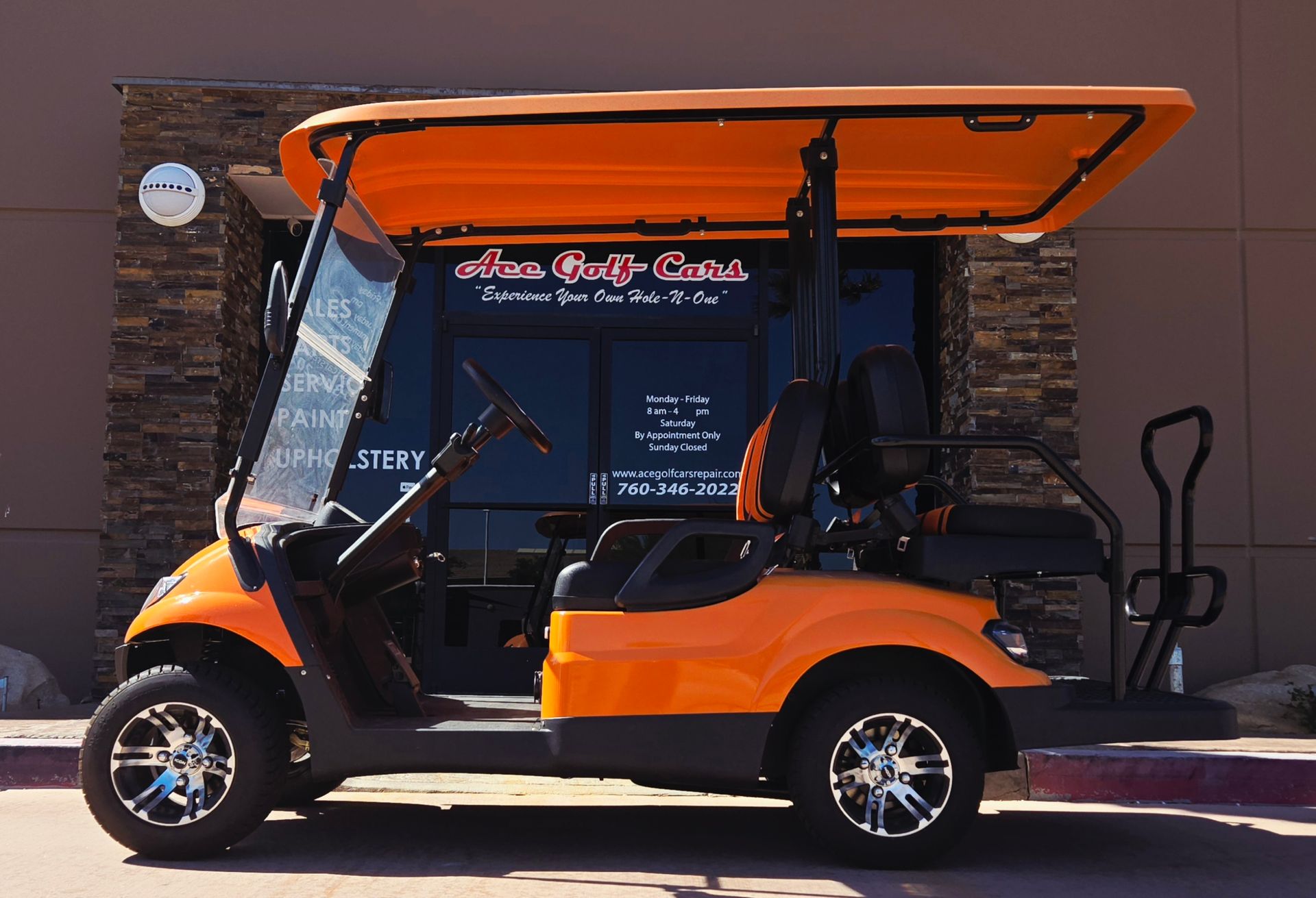 An orange golf cart is parked in front of a store that sells golf carts