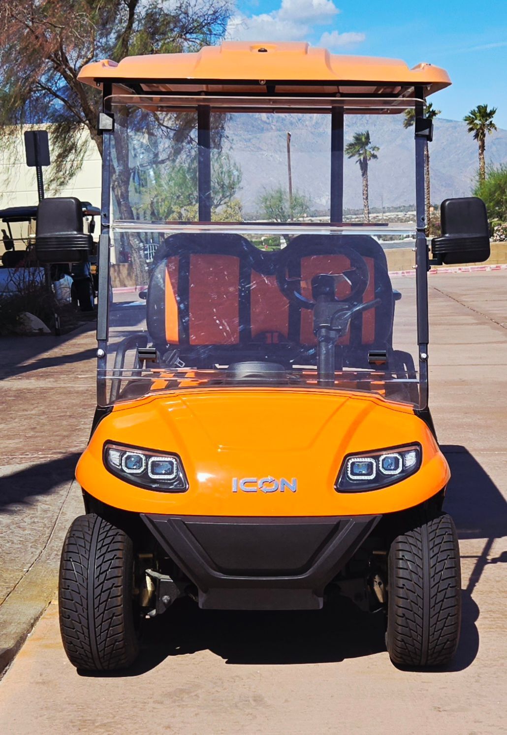 An orange golf cart is parked on the side of the road.