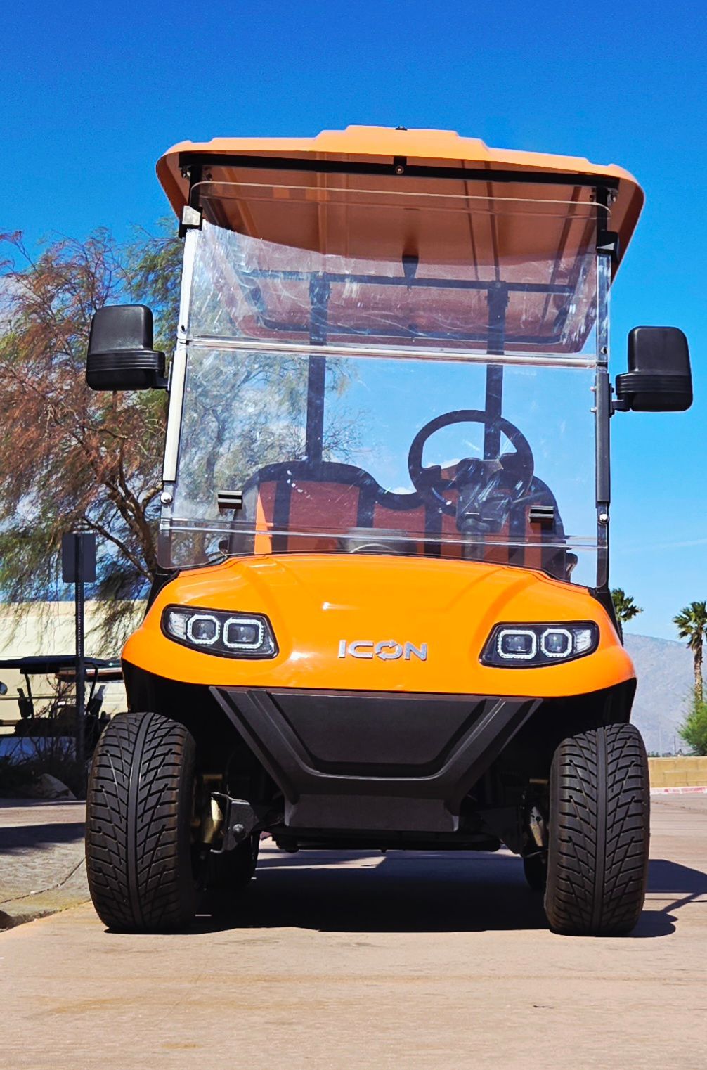 An orange golf cart is parked on the side of the road.