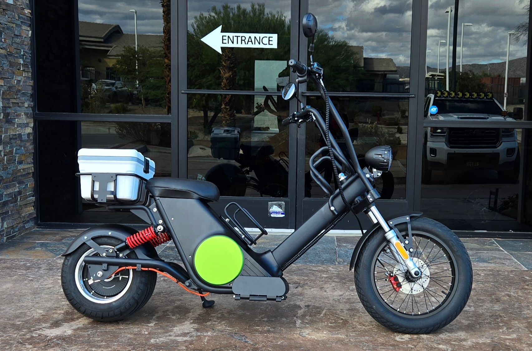 Black electric scooter with a green accent parked outside an entrance with glass doors.
