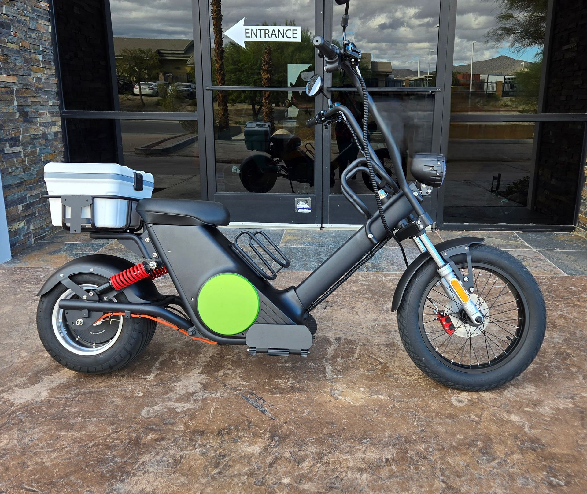 Black electric motorcycle with white storage box, parked outside a building.