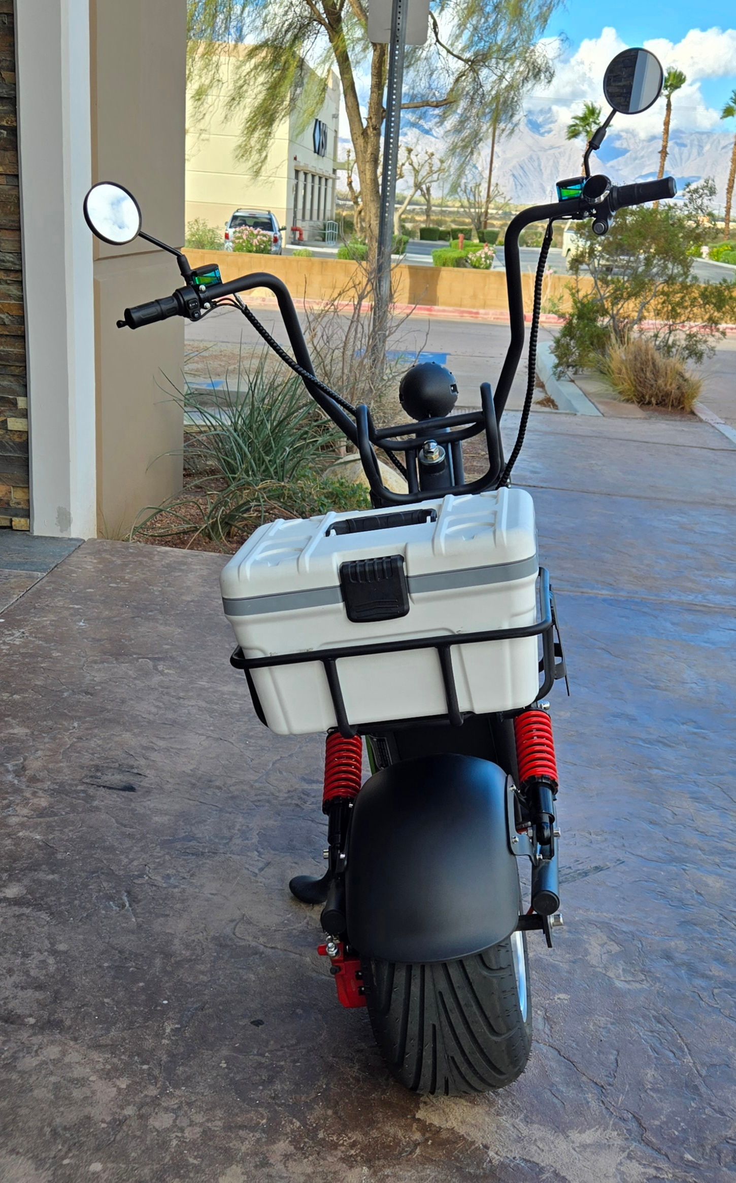 Black electric scooter with white storage box, red shocks, on concrete.
