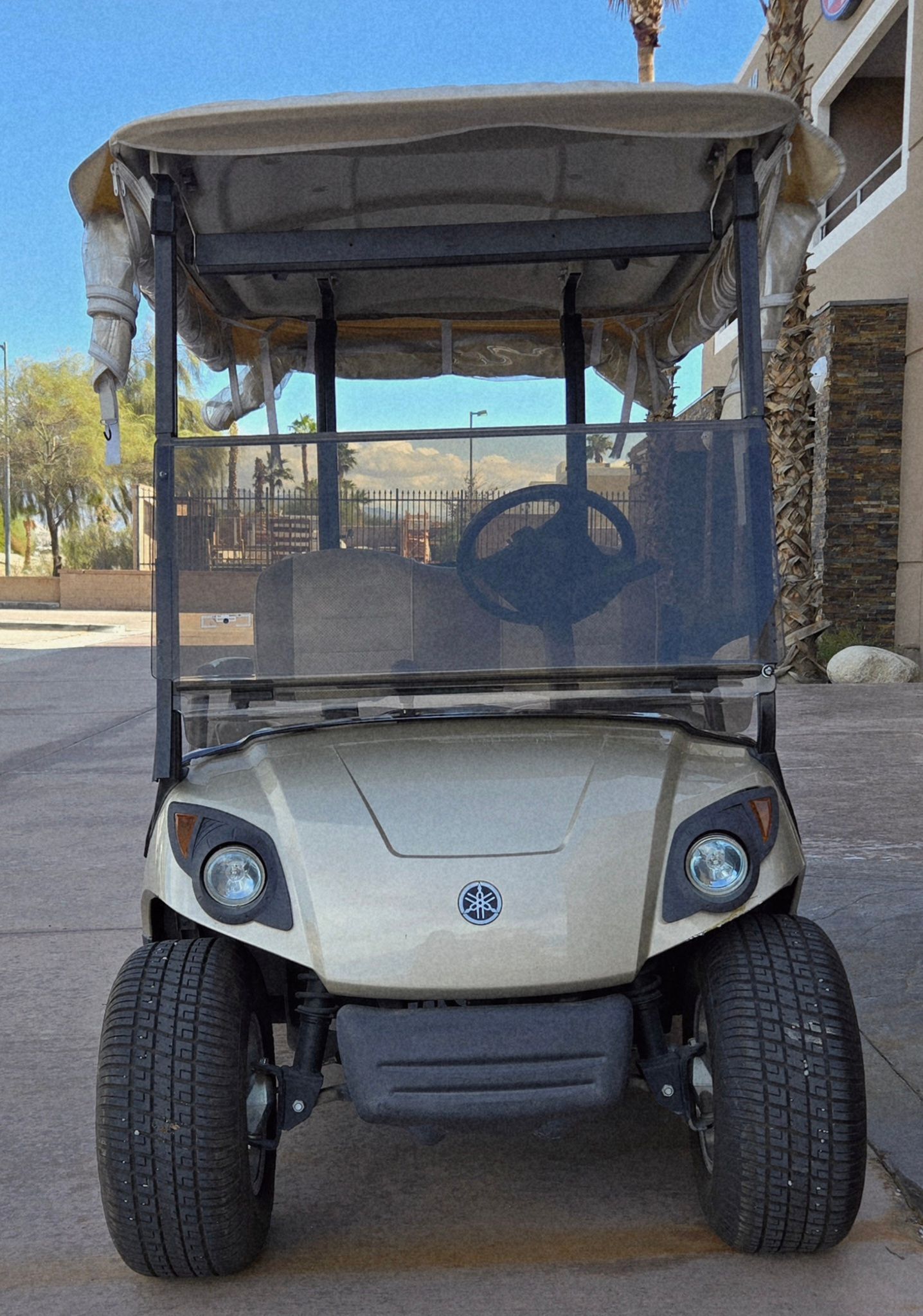 Tan golf cart with black tires and windshield, parked outdoors.