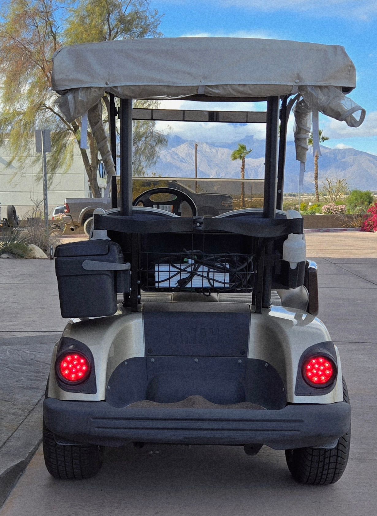 Rear view of a beige golf cart with a canopy, displaying red taillights, parked outside on pavement.