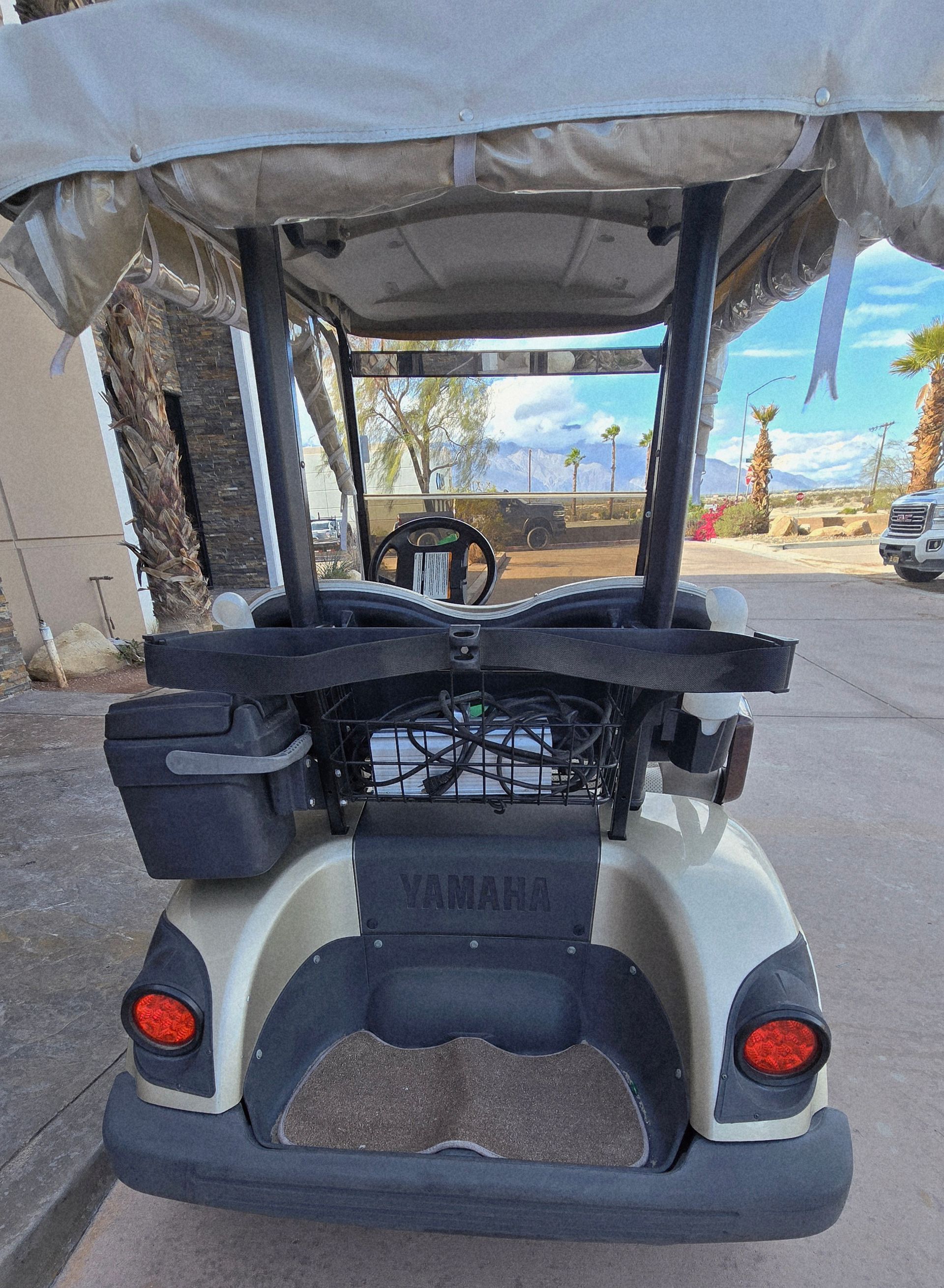 Rear view of a beige and black Yamaha golf cart with a windshield, parked on a paved road.