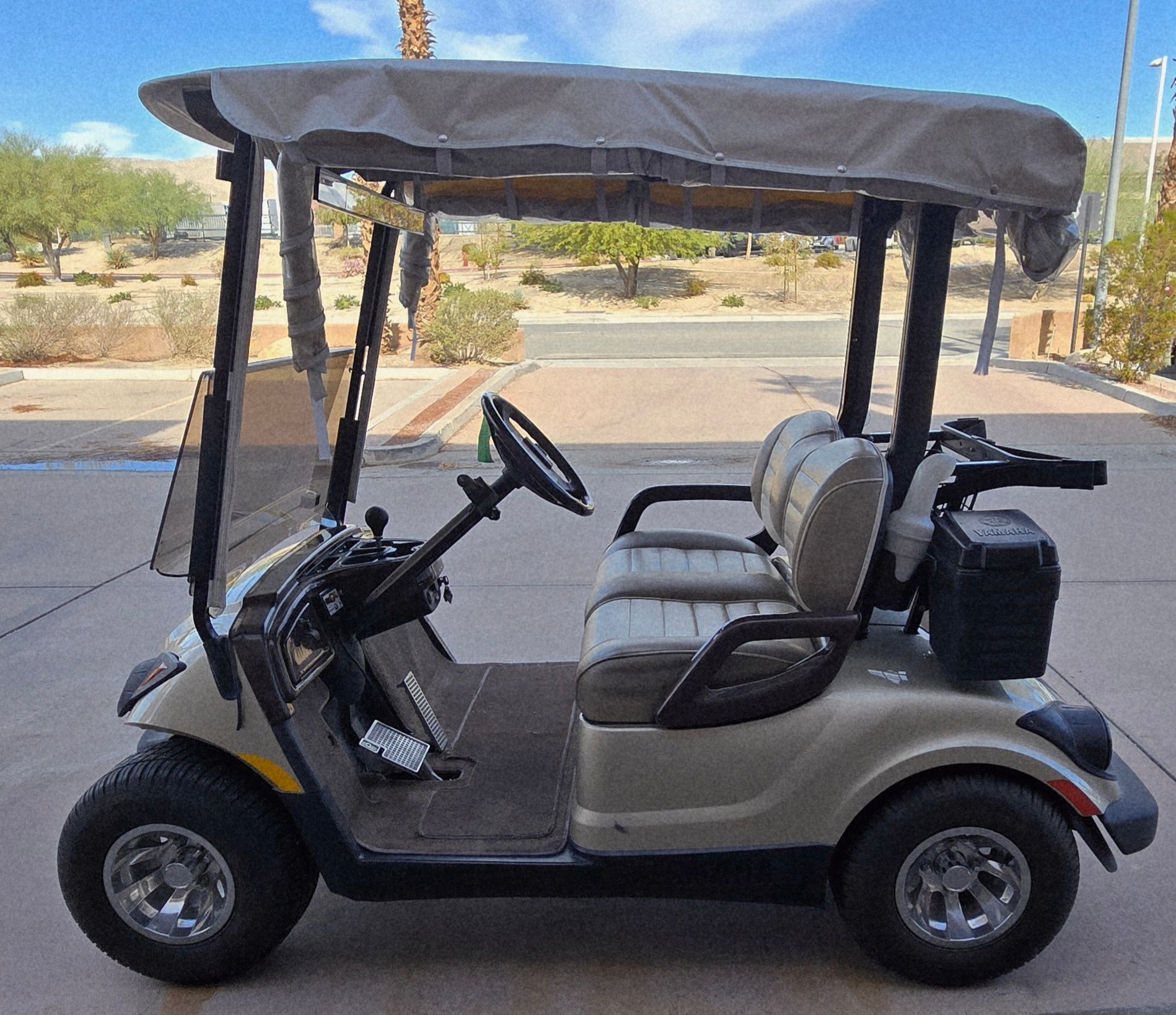 Tan golf cart with roof, seats, and windshield parked outdoors.