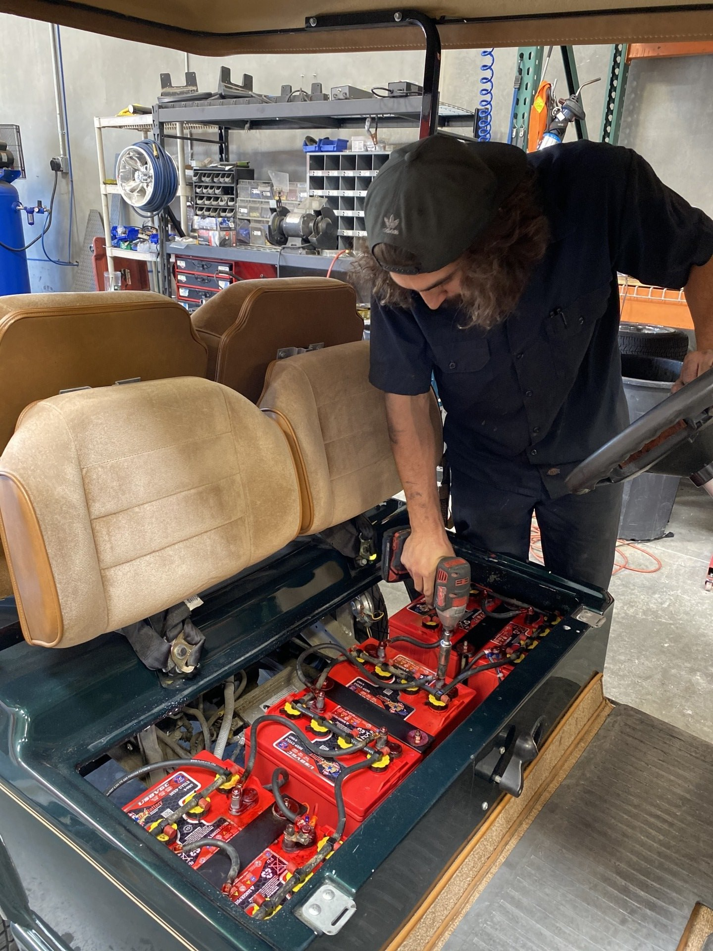 A man is working on a golf cart with a drill.