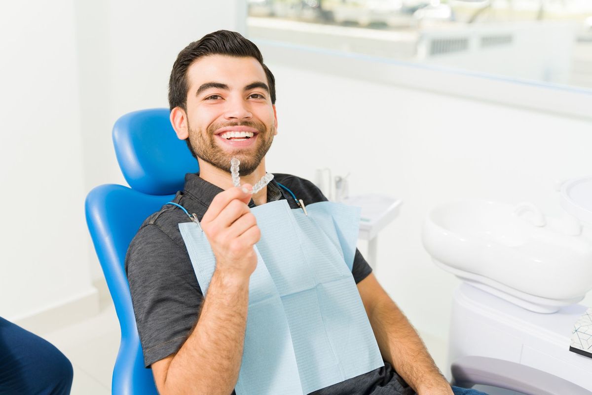 Man smiling holding a Invisalign mouth piece