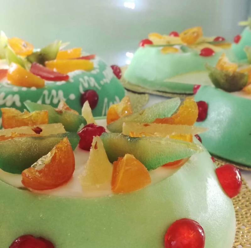 Piccole tortine verdi rotonde, ricoperte di frutta candita e bacche rosse.