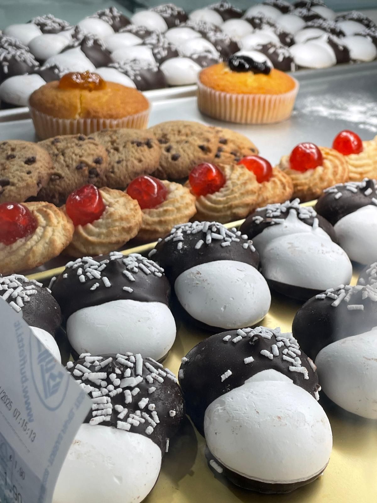 Esposizione di vari tipi di dolci: muffin, biscotti e biscotti bianchi e neri con granella e ciliegie.