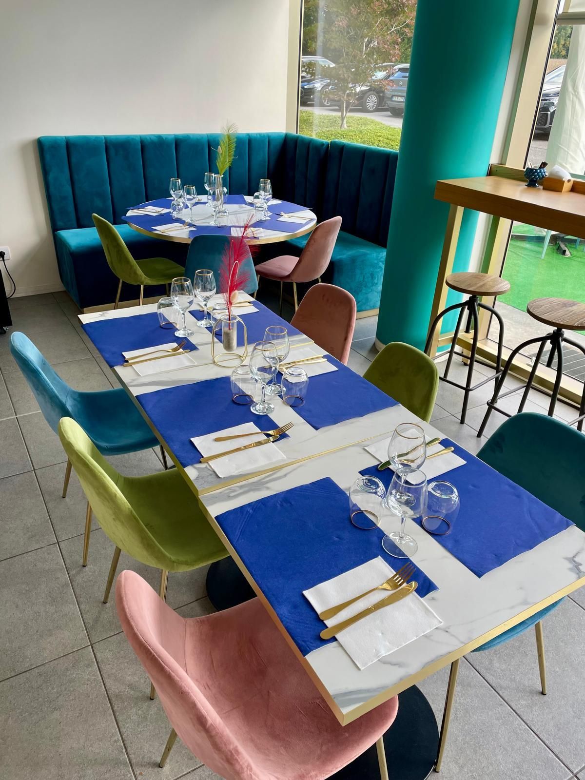 Interno del ristorante: sedute blu, rosa e verdi attorno ai tavoli apparecchiati per la cena, vicino a un pilastro verde acqua.