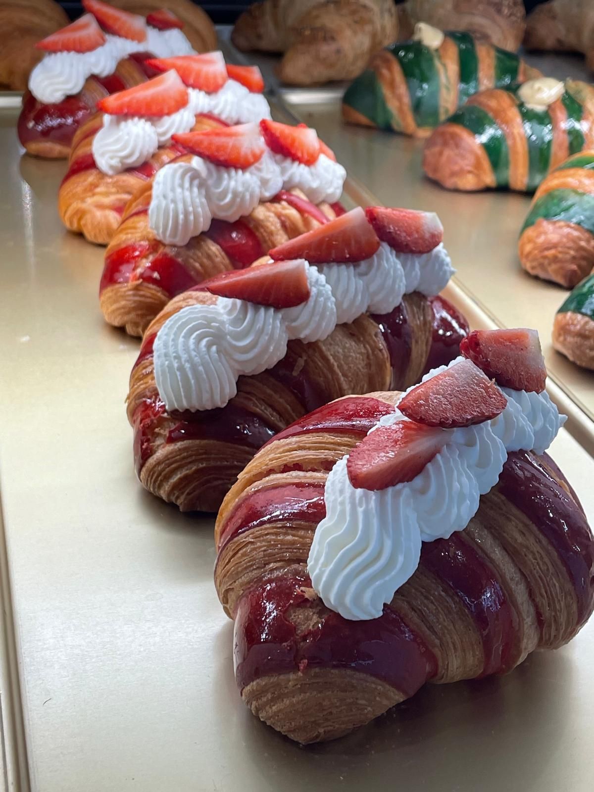 Cornetti ricoperti di panna montata e fragole a fette, glassati di rosso su un vassoio.