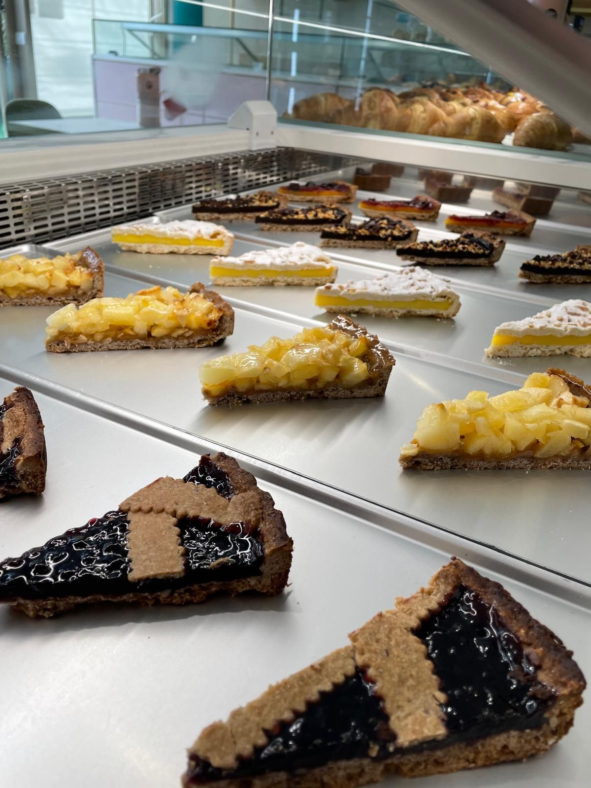 Vetrina di crostate: fette di mela, limone e frutti di bosco su ripiani di metallo.