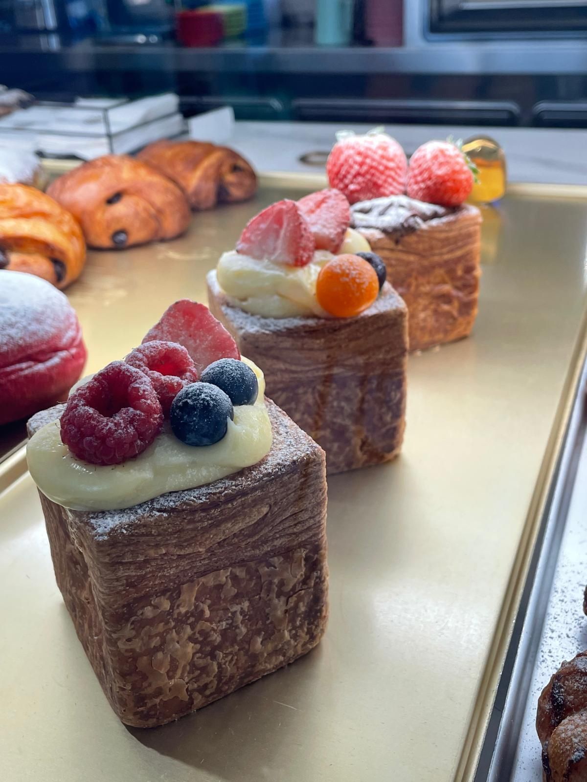 Vetrina con pasticcini, tra cui pasticcini a strati a forma di cubo ricoperti di frutti di bosco e zucchero a velo.
