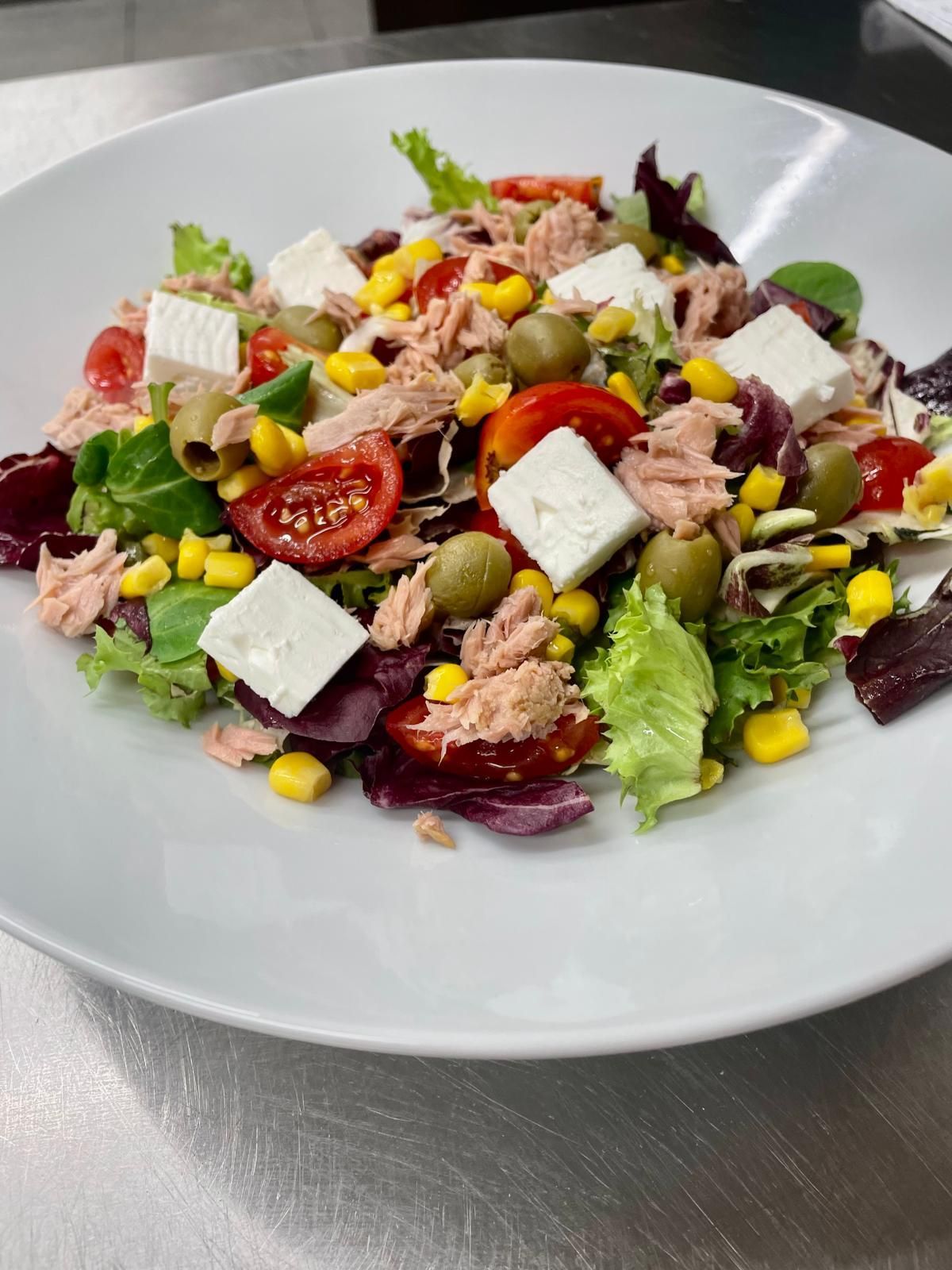 Insalata con tonno, feta, mais, pomodori e olive su un piatto bianco.