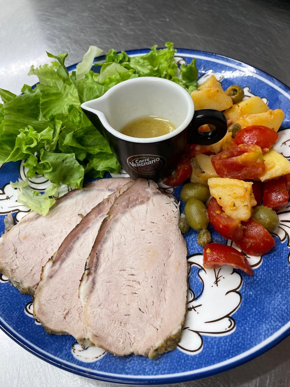 Piatto di carne affettata con insalata, insalata di patate, olive e condimento in una piccola tazza su un piatto blu.