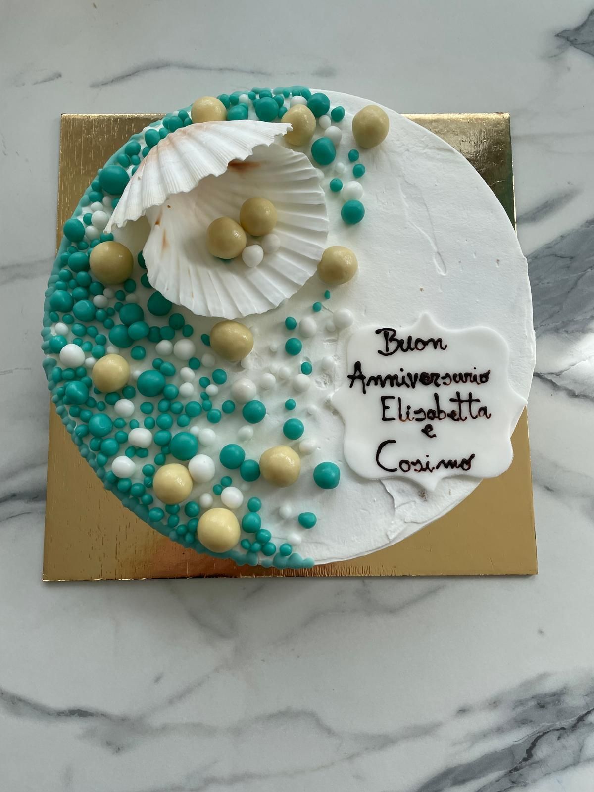 Torta decorata con perle commestibili color turchese e oro, conchiglia e scritta 