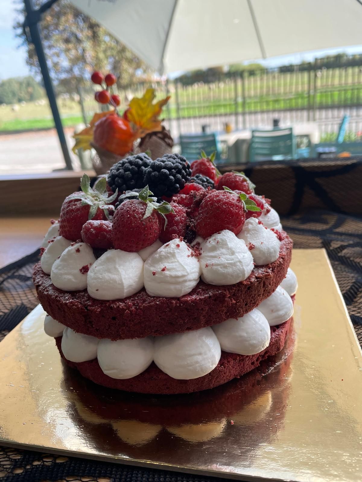 Torta red velvet con panna montata e frutti di bosco su una superficie dorata; ambientazione esterna.