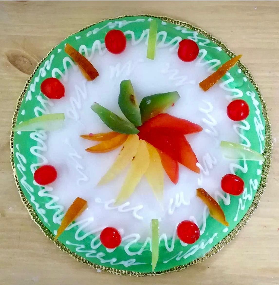 Torta decorata con frutta, bordo di glassa verde e linee decorative.