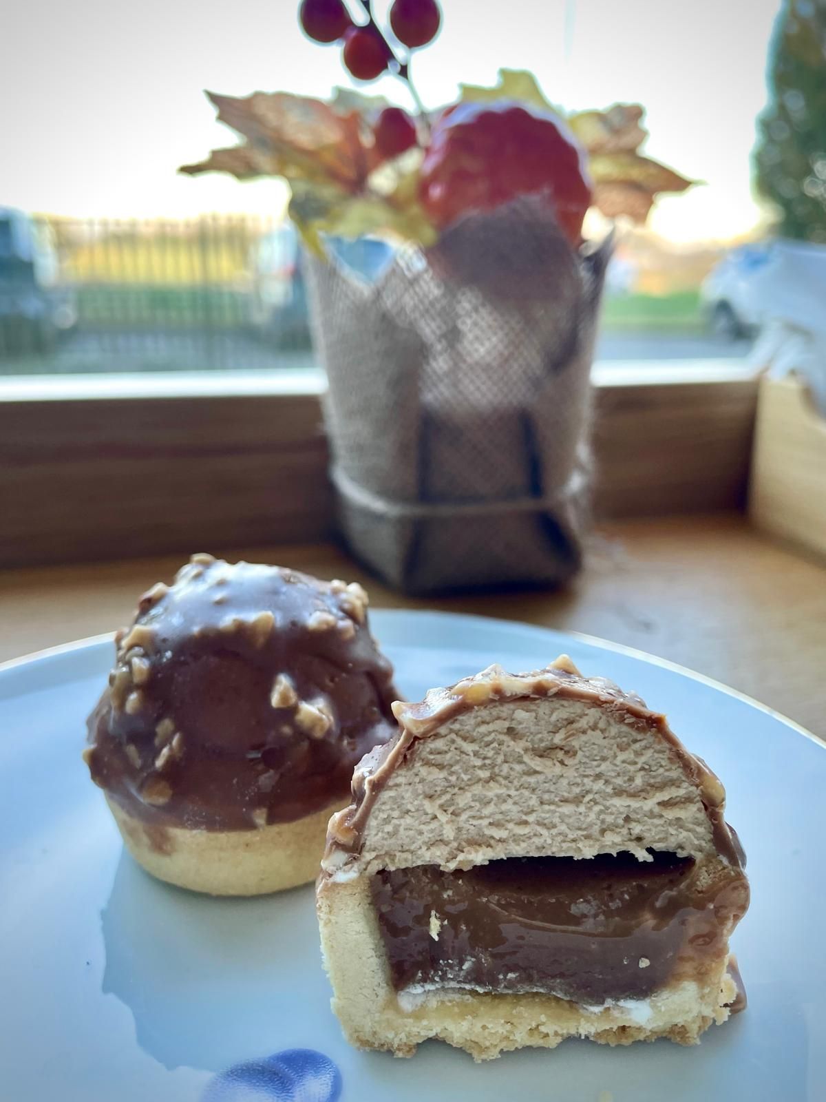Pasta sfoglia al cioccolato con ripieno al caramello, tagliata a metà. Presentata su un piatto, con decorazioni autunnali sullo sfondo.
