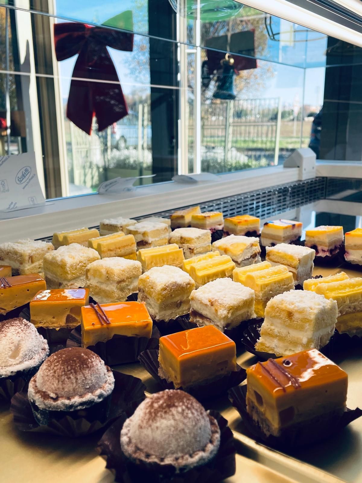 Vetrina con file di pasticcini colorati, tra cui cubetti e sfere di cioccolato.