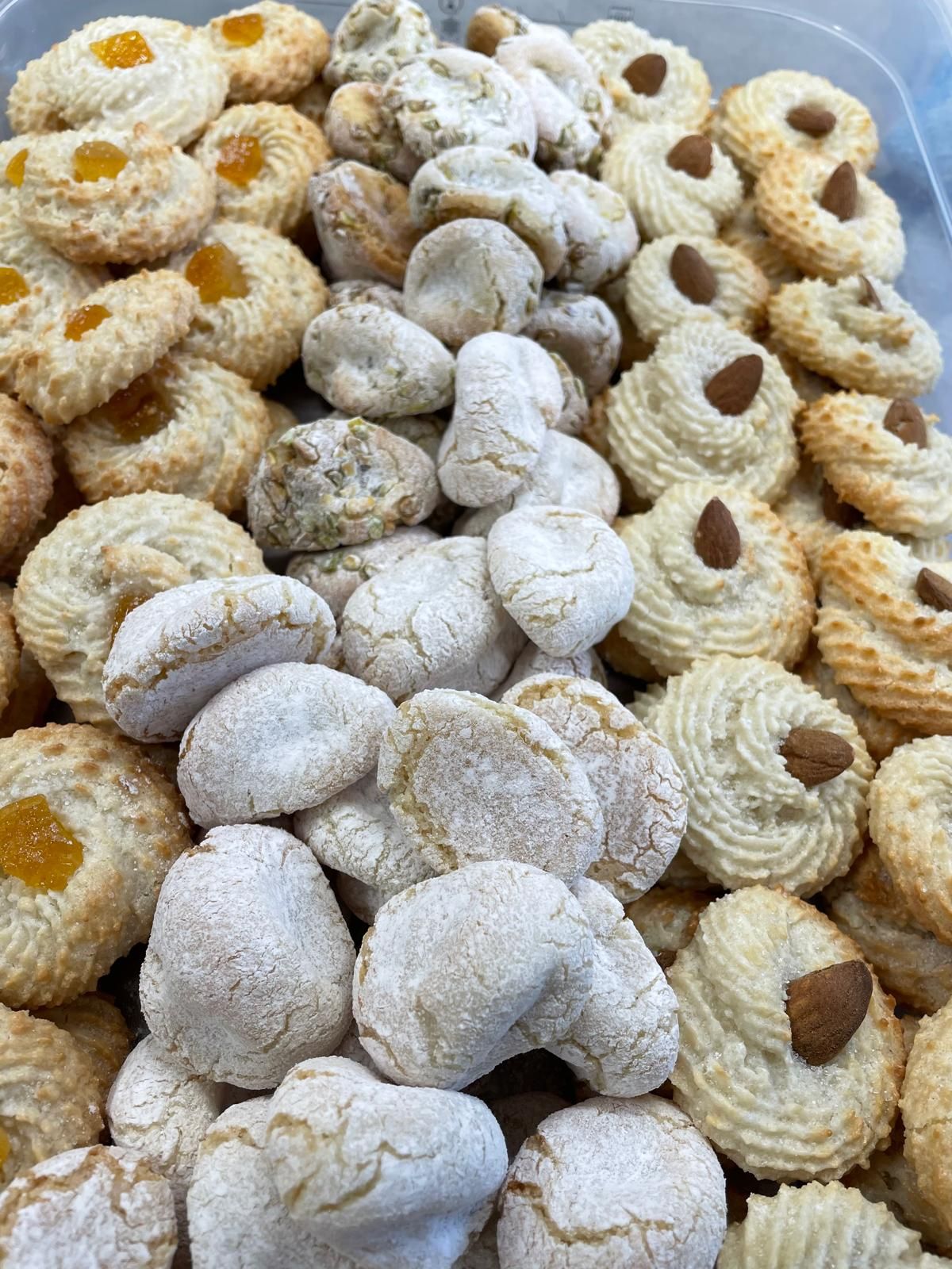 Mucchio di biscotti di vario tipo, tra cui quelli rotondi e quelli sagomati, con guarnizioni come mandorle e marmellata, in colori chiari.
