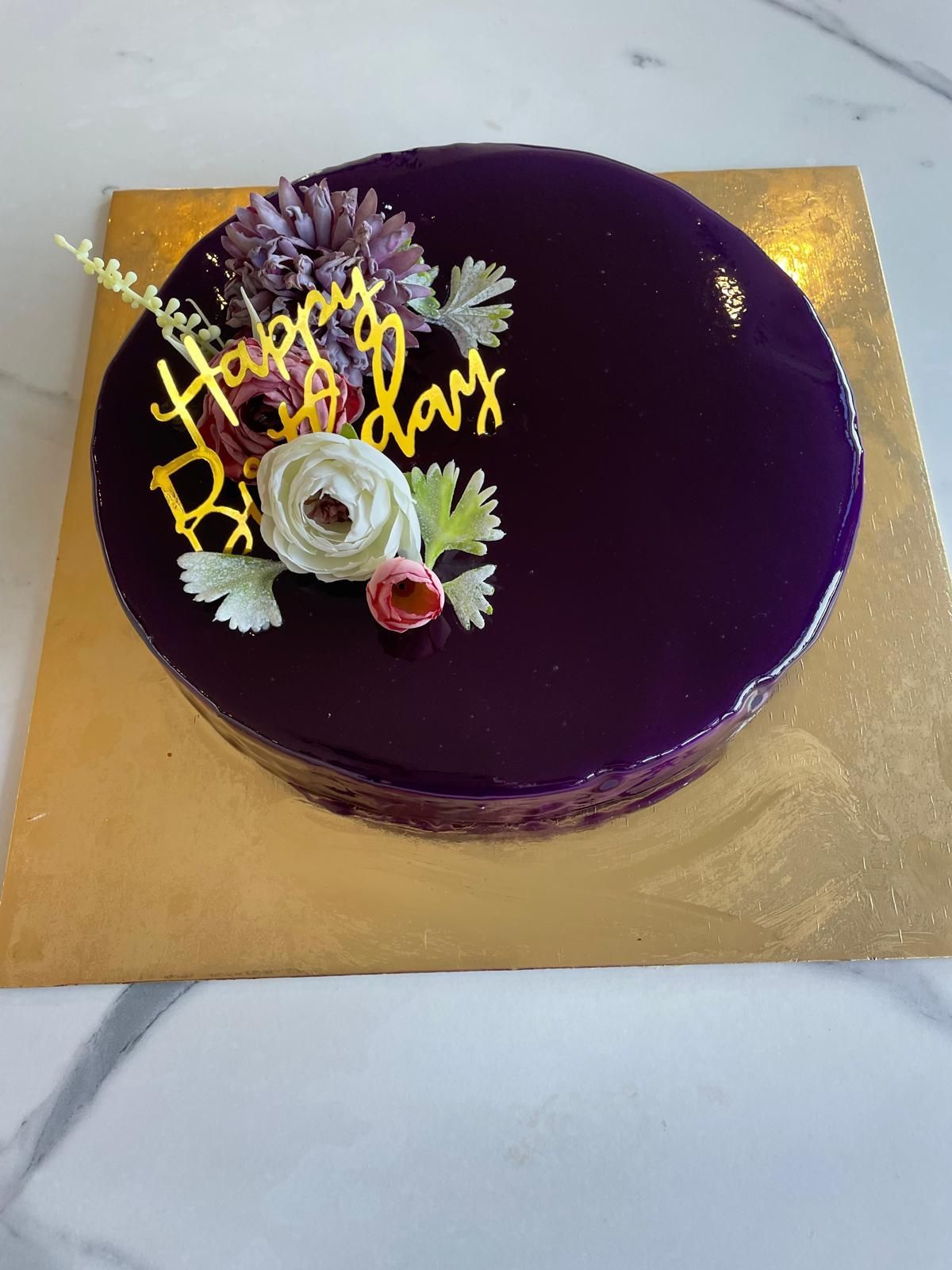 Torta di compleanno glassata viola con decorazioni floreali e topper con la scritta 