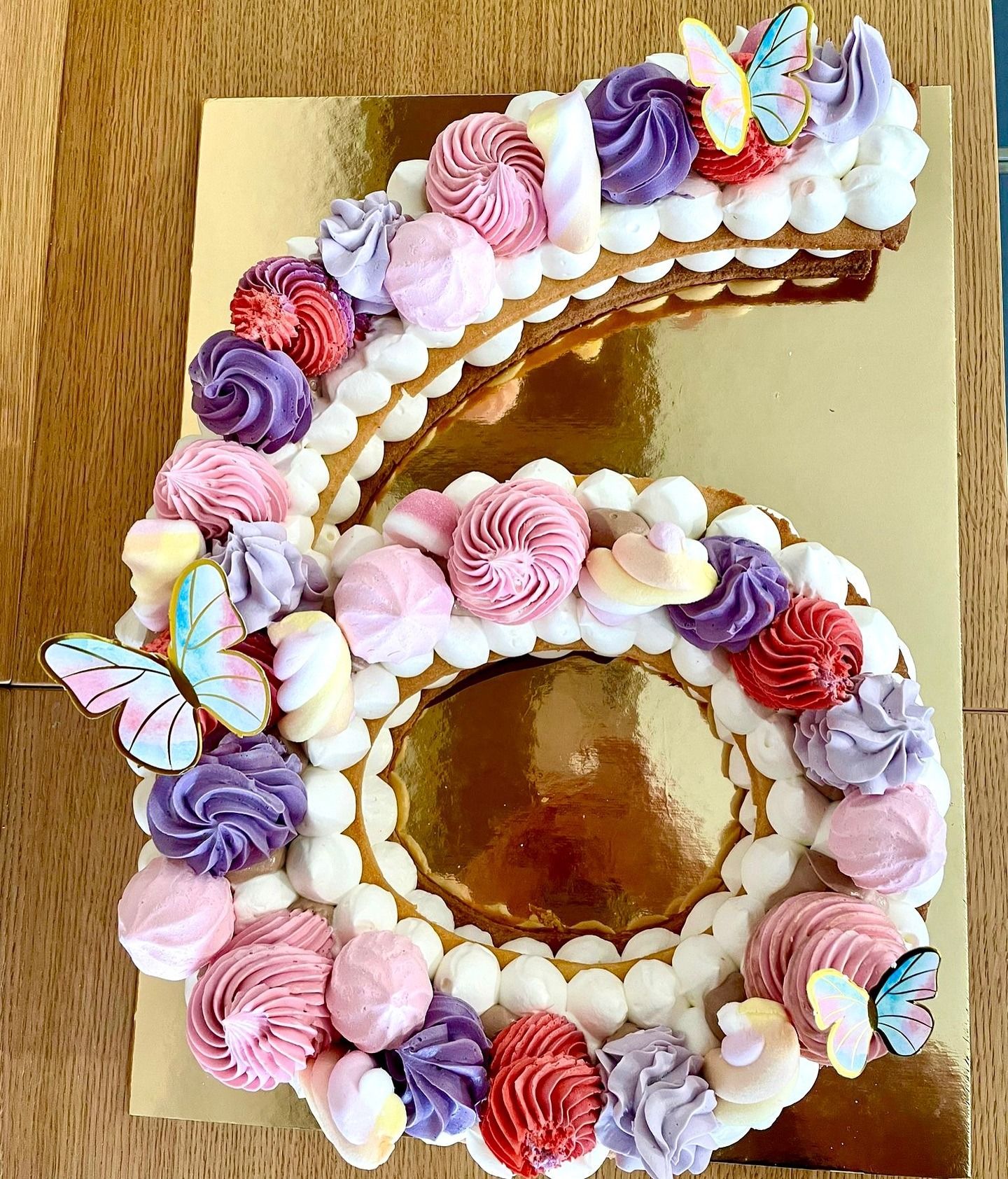Torta di compleanno a forma di numero sei, decorata con glassa, meringhe e farfalle.