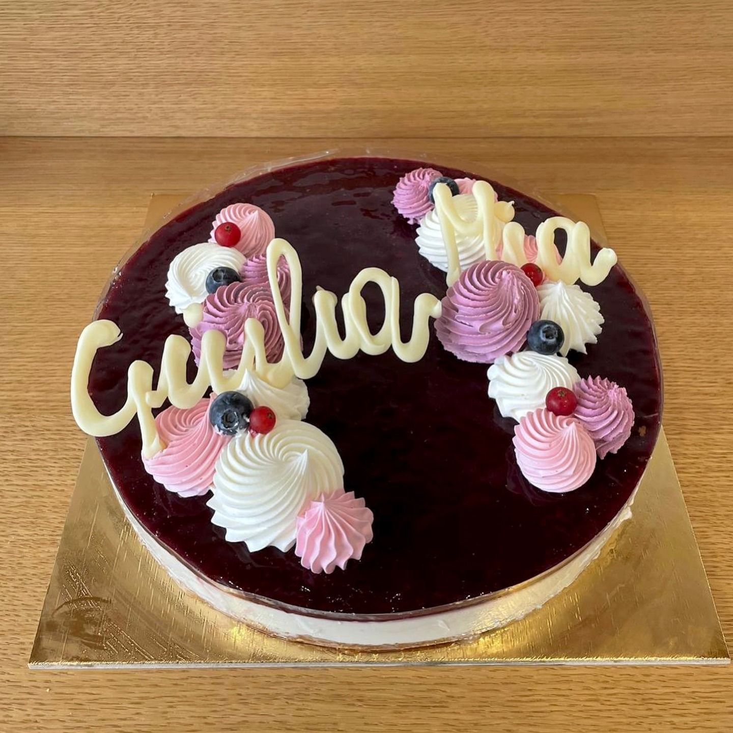 Torta rotonda con glassa viola scuro, spirali di glassa bianca e la scritta "Giuliana" scritta in glassa bianca.